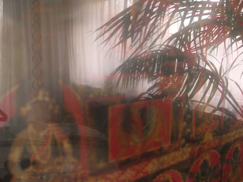 Bild eines tibetischen Tangka mit einer yogischen Sitzhaltung, mit Spiegelung von Fenster & Palmblttern